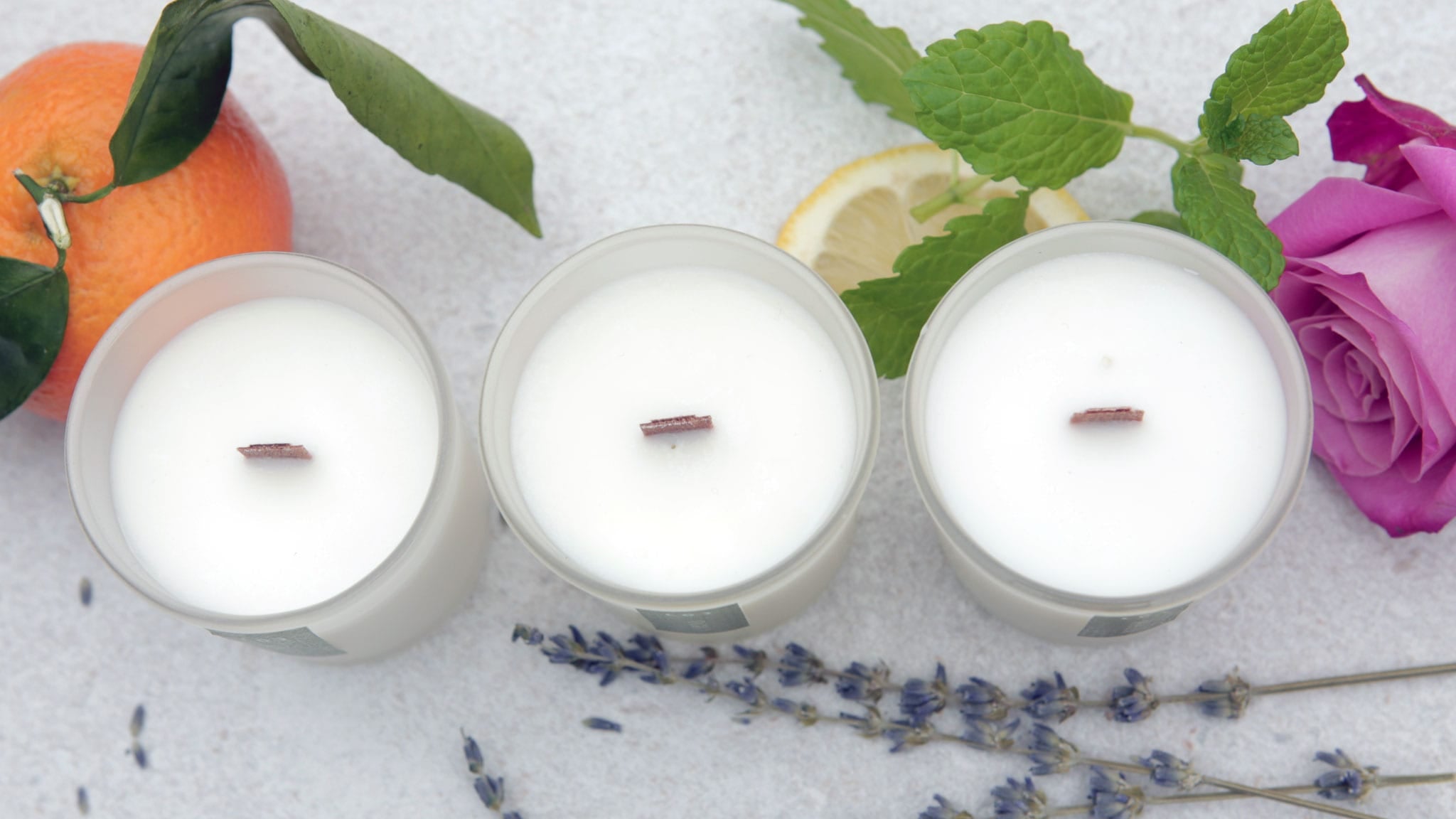 Three natural scented candles with wood wicks in frosted glass jars with an orange, lemon, lavender sprig and pink rose | Scooms