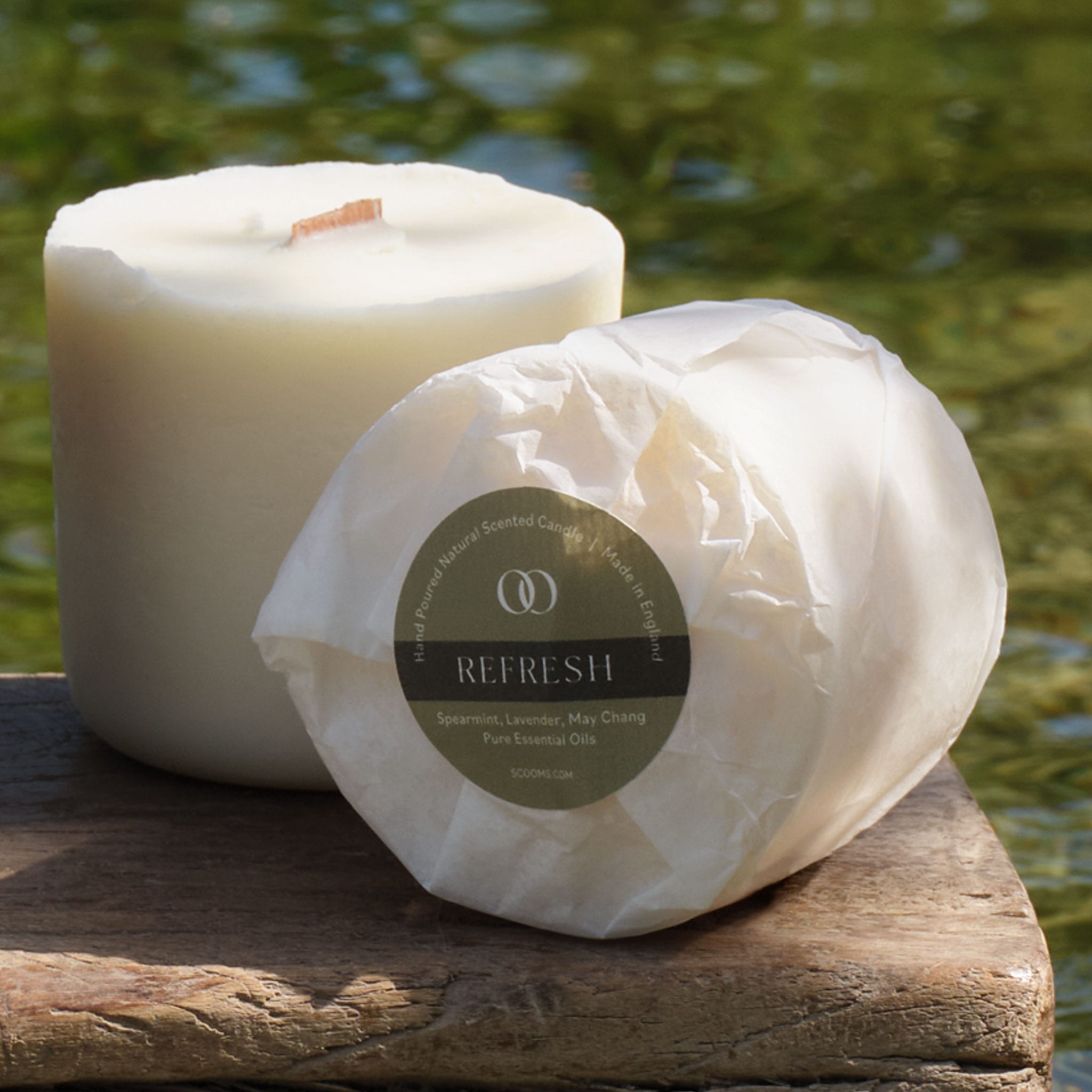 Two natural scented candle refills wrapped in paper, set on a rustic wooden board with a blurred green water background. | Scooms