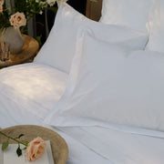 White percale Egyptian cotton bed linens with pillowcases and a white sheet, styled with a woven tray holding a book and a peach rose. | Scooms