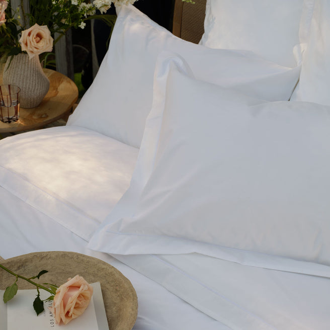 White percale Egyptian cotton bed linens with pillowcases and a white sheet, styled with a woven tray holding a book and a peach rose. | Scooms