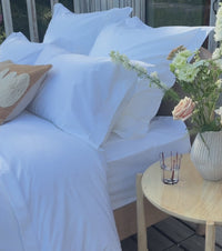 White percale Egyptian cotton bed linens with pillowcases and a white sheet, styled with a woven tray holding a book and a peach rose. | Scooms
