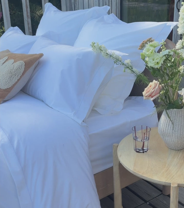 White percale Egyptian cotton bed linens with pillowcases and a white sheet, styled with a woven tray holding a book and a peach rose. | Scooms
