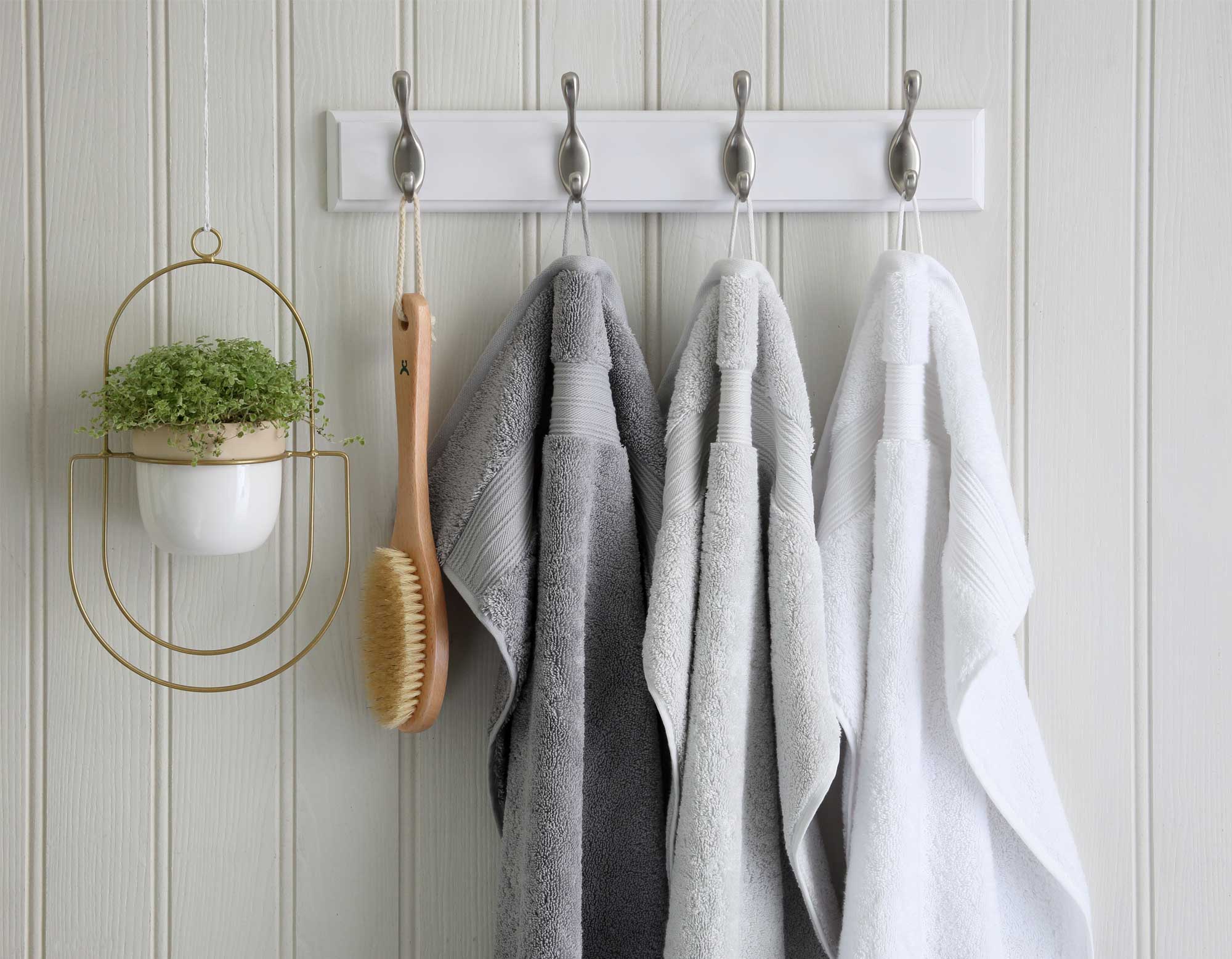 Egyptian cotton bath towels in white and grey hanging from hooks on wall
