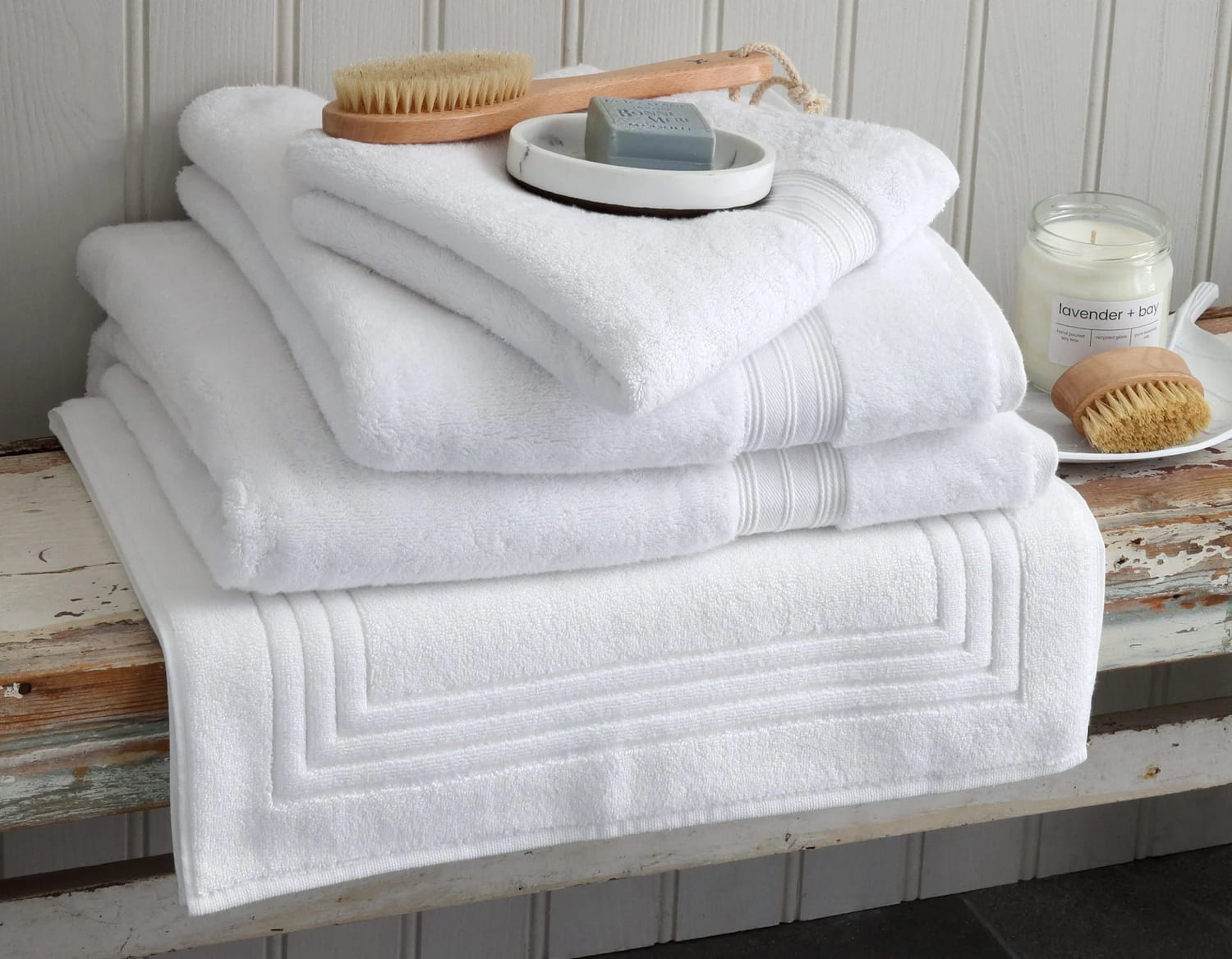 Bundle of white bath towels on rustic bench with scrubbing brush and scooms candle