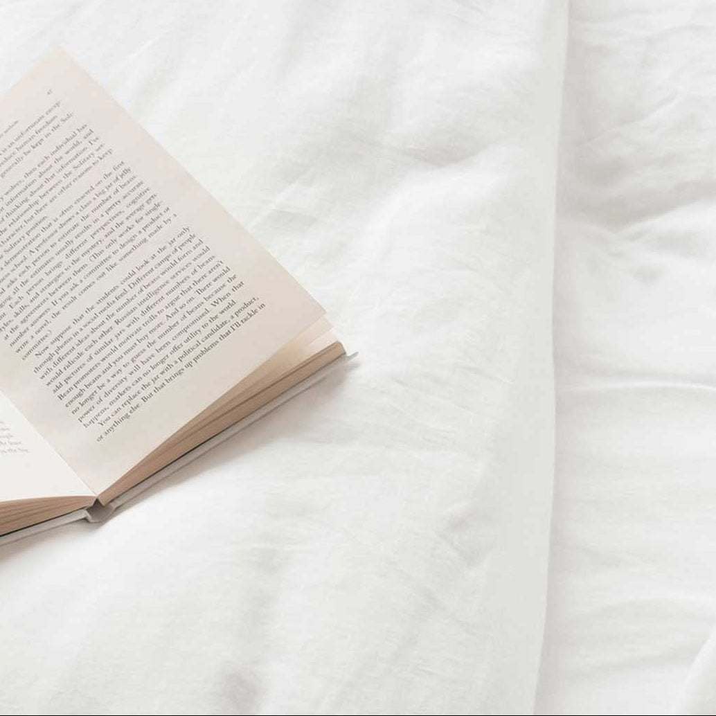 White linen sheets and covers close up with open book | Scooms
